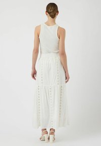 Witte maxi rok met gelaagd ontwerp, geborduurde accenten en elastische tailleband. Draagt met een aansluitend wit tanktop en sandalen met hakken en bandjes.