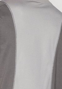 Veste de sport grise et argentée avec un design en blocs de couleur, texture lisse et coutures contrastées. Vue de dos présentée.