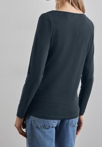 Långärmad mörkgrå skjorta med rund halsringning. Mjuk bomullstextur, figursydd design och ren fåll, tillsammans med ljusblå jeans.