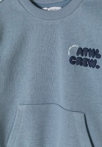 Lichtblauwe sweater met ronde hals, gemaakt van zacht materiaal, met een voorzak en geborduurd "ATHL CREW." logo in donkerblauw.