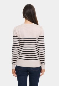 Randig tröja i ljusbeige med svarta horisontella ränder. Har en ribbad halsringning och ärmar samt en åtsittande midja. Standard design bak.