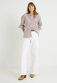 Camisa de rayas tipo button-up con mangas enrolladas, combinada con jeans blancos de campana y botines de ante beige con tacón. Detalles de costura visibles.