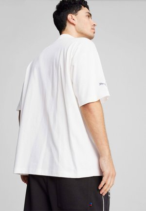 Camiseta blanca de algodón de manga corta con un ajuste relajado, que presenta un pequeño logo en la manga izquierda y una textura suave.