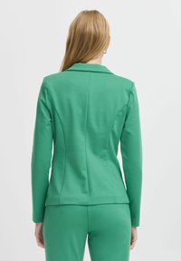Groene op maat gemaakte blazer met lange mouwen, voorzien van een reverskraag en rugnaden, gemaakt van een zachte, elastische stof.