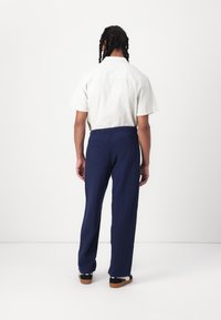 Chemise à manches courtes rayée claire avec une coupe décontractée, associée à un pantalon bleu marine ample. L'ensemble présente un design simple et un tissu respirant.