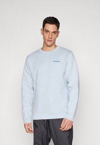 Sweatshirt albastru deschis din material moale, cu guler rotund și un mic logo brodat în zona stângă a pieptului.