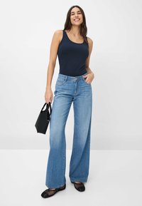 Top aderente di un blu scuro abbinato a jeans a gamba larga di un blu chiaro, ballerine in rete nere e una piccola borsa nera. Tessuto morbido e forma rilassata.
