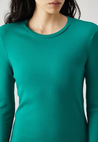 Τιρκουάζ μακρυμάνικη μπλούζα από ριμπ ύφασμα με στρογγυλή λαιμόκοψη, που διαθέτει κατακόρυφες ρίγες και κολλητή σιλουέτα.