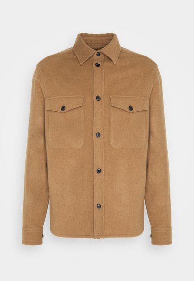 Brun ullblanding skjortejakke med spiss krage, svarte knapper, to brystlommer og rett snitt. Myk tekstur, minimalistisk design.