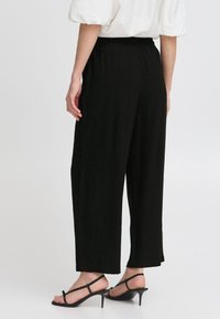 Schwarze weite Hosen mit elastischem Bund, die eine glatte Textur und ein sauberes Design aufweisen. Kombiniert mit schwarzen Riemchenschuhen.