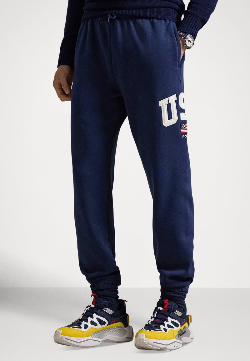 Marineblaue Jogginghose mit elastischem Bund und Bündchen, mit weißem "U.S."-Logo und einem kleinen amerikanischen Flaggen-Detail an der Seite.
