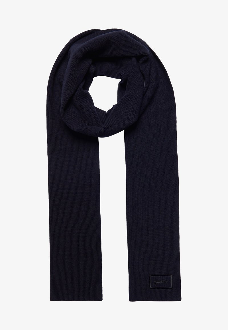 Écharpe en laine tricotée bleu marine foncé, pliée avec une petite étiquette en tissu rectangulaire cousue près d'une extrémité.