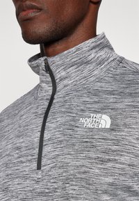 Grauer, strukturierter Fleece-Pullover mit Viertel-Reißverschluss am Kragen. Verfügt über ein weißes Logo auf der Brust und eine angeraute Oberfläche für zusätzliche Wärme.