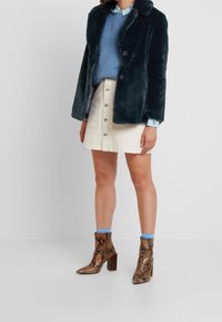 Tumman tealinsininen tekoturkistakki, vaaleansininen kuvioitu neulepaita, kermanvärinen denimhame napituksella ja ruskeat käärmekuvioiset nilkkurit paksulla korolla.