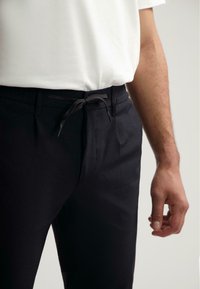 Pantalons noirs avec une finition texturée, dotés d'une taille à cordon et de poches latérales. Associés à un t-shirt blanc à manches courtes.