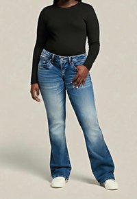 Niebieskie dzwonowe dżinsy o średnim odcieniu, z pięcioma kieszeniami, kontrastowym przeszyciem i srebrnym guzikiem, zestawione z czarną, długorękawową bluzką.