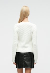 Pull blanc tricoté avec un motif texturé en losange, manches longues et encolure ronde, associé à une mini jupe en cuir noir.