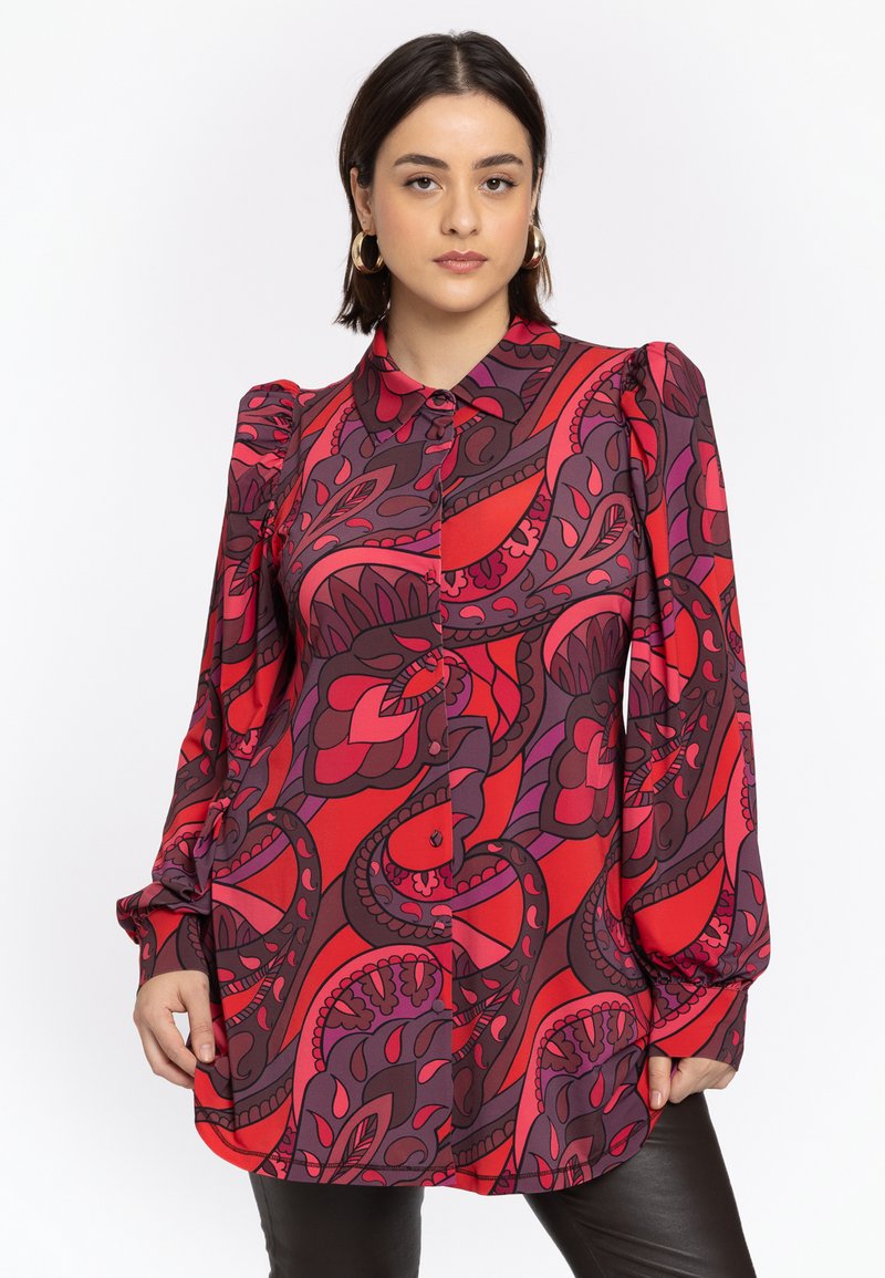 Rode en paarse gebloemde blouse met een knoopsluiting aan de voorkant, geplooide mouwen en een gebogen zoom. Gemaakt van gladde stof met bloemvormen.