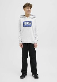Felpa grigia chiara con logo grafico blu, abbinata a pantaloni neri e sneakers nere. Caratterizzata da cappuccio con coulisse e polsini a costine.