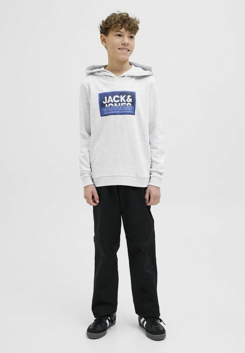 Felpa grigia chiara con logo grafico blu, abbinata a pantaloni neri e sneakers nere. Caratterizzata da cappuccio con coulisse e polsini a costine.