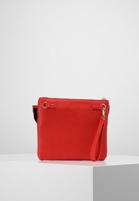 Rød lædertaske med lynlåslukning, flad form og kort håndledsrem. Har guldfarvede metaldele og glat tekstur.