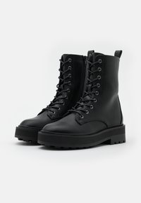 Botas de tobillo de cuero negro con suela de plataforma gruesa, con cierre de cordones y cremallera lateral, superficie texturizada y ojales plateados.
