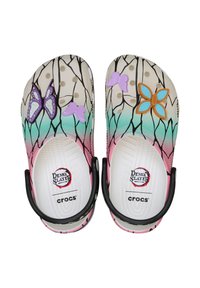 Par de zapatos Crocs con patrón de ramas de árbol negras, tonos degradados de rosa y verde, decorados con charms de mariposas moradas y azules.