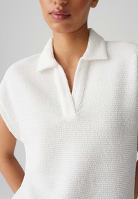 Polo shirt bianco in tessuto testurizzato con un morbido tessuto a boucle, dotato di un colletto e maniche corte.