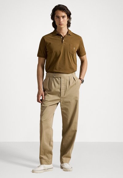 Brown polo shirt with short sleeves and a chest pocket, paired with light beige pleated trousers and white sneakers. Simple design and fit.