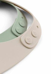 Kaks painduva päikeseprilli, üks heledas beežis ja teine summutatud rohelises, millel on nööpfikseerimisdetailid ja ümmargused logo aksessuaarid. Sile, matte viimistlus.