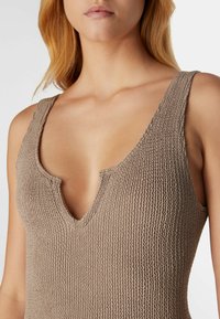 Braun strukturiertes Strickoberteil mit tiefem V-Ausschnitt und breiten Schulterträgern. Der Stoff wirkt weich mit einem durchgehenden Rippenmuster.