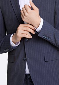 Marinblå randig kavaj med knappstängning, matchande knappar på ärmsluten och en bröstficka. Den inre skjortan har en vit krage.