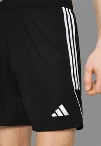 Zwarte sportshorts met witte zijstrepen en logo, gemaakt van glad materiaal; heeft een elastische tailleband en een comfortabele pasvorm.