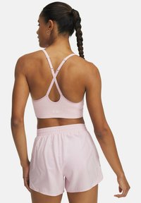 Sujeción deportiva de color rosa claro con un diseño de espalda en cruz, combinada con un pantalón corto rosa claro a juego con una cinturilla elástica.