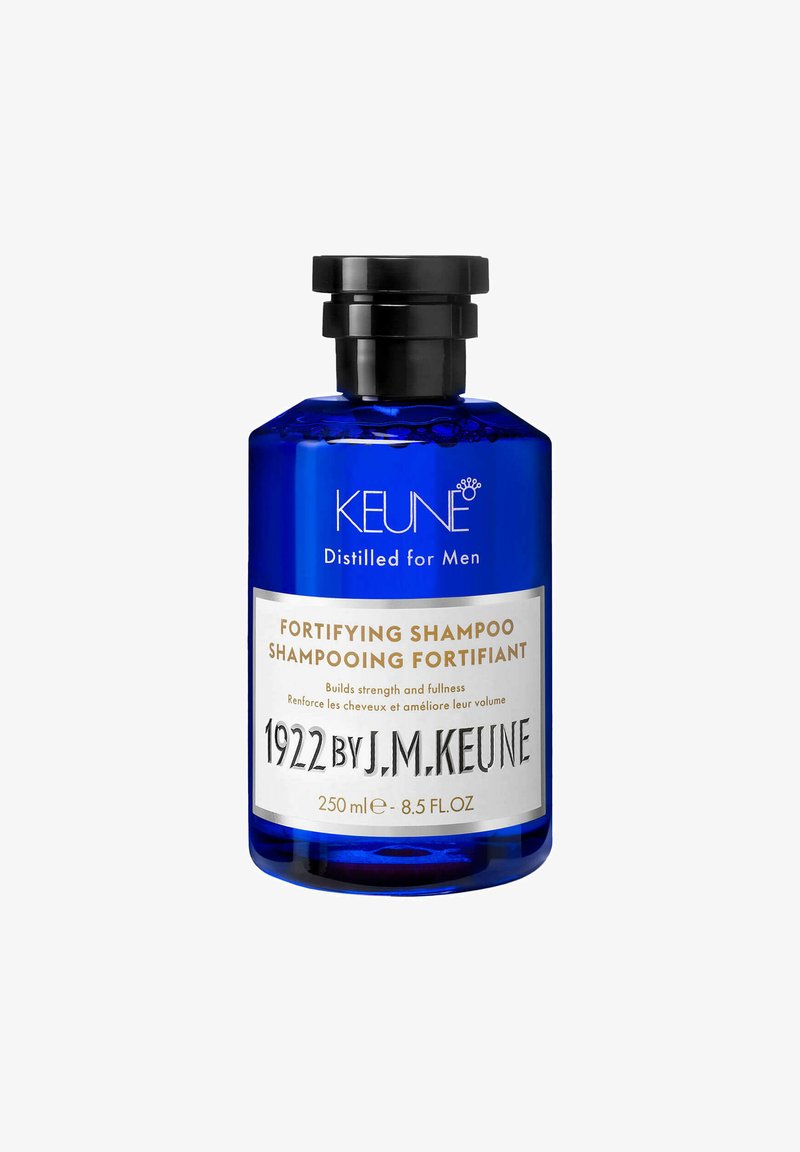 Bouteille en verre bleue avec un capuchon noir. L'étiquette présente un texte blanc, indiquant "Shampooing Fortifiant" et "1922 par J.M. Keune," taille 250 ml.