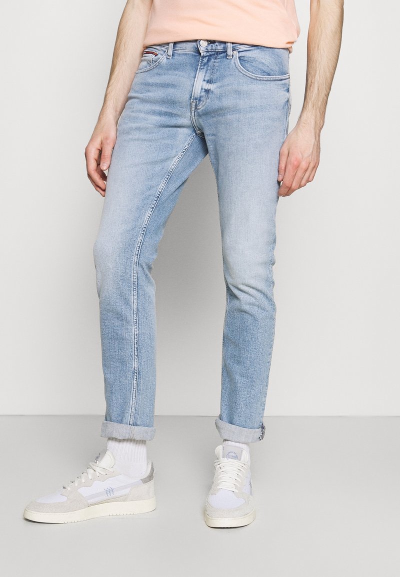 Hellblaue Denim-Jeans mit Slim Fit, leichter Abnutzung und umgeschlagenen Säumen, kombiniert mit weißen und grauen Sneakers.