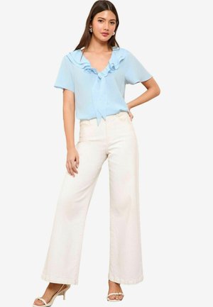 Light blue blouse with ruffled neckline and tie, paired with high-waisted white wide-leg pants. Model wears strappy beige heels.