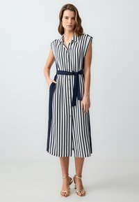 Ärmelloses, knielanges Hemdkleid mit senkrechten Streifen in Marineblau und Weiß, Stoffgürtel, seitlichen Taschen und einem Saum bis zum Knie.