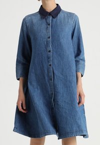 Denimklänning med mörkblå krage, långa ärmar och knäppning fram. Lätt utsvängd design med knälång fåll.