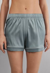 Světlé zelené saténové šortky s elastickým pasem a bílými lemy. Mají uvolněný střih a ohrnuté manžety pro jemný siluetu.