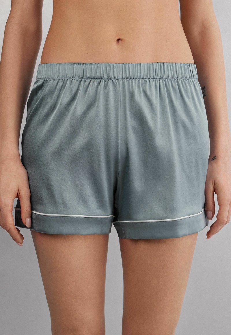 Světlé zelené saténové šortky s elastickým pasem a bílými lemy. Mají uvolněný střih a ohrnuté manžety pro jemný siluetu.