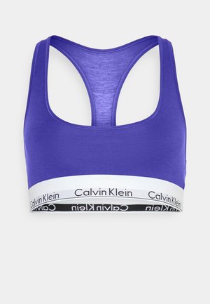 Violet sporta krūšturis, kas izgatavots no mīksta auduma, ar racerback dizainu, platu elastīgu jostu, kurai ir balta un melna "Calvin Klein" logo detaļa.