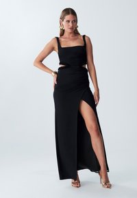 Black sleeveless maxi dress featuring a square neckline, ruched detailing, cut-out accents, and a thigh-high slit. Smooth fabric texture.
