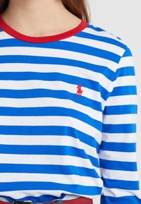 Blå och vit randig långärmad skjorta med röd krage och en liten röd broderad logga på bröstet. Mjuk tygkvalitet, avslappnad passform.