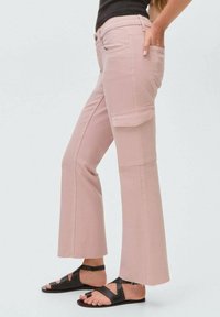 Roze cargobroek met een rechte pijp ontwerp, voorzien van zijzakken en ruwe zoomdetails. Gedragen met zwarte sandalen met bandjes.