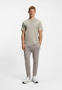 Hellgraues Kurzarm-T-Shirt mit Rundhalsausschnitt und dezentem horizontalem Streifenmuster. Kombiniert mit grauen, zulaufenden Jogginghosen und weißen Sneakers.