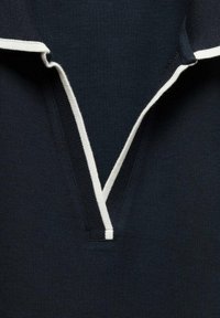 Námořnická polo košile s žebrovaným límcem a bílými akcenty, ve tvaru V. Textura vypadá hladce s pleteným vzorem.