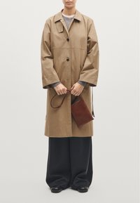 Beżowy, oversize płaszcz z szerokimi rękawami, z zapięciem na jeden guzik, noszony na szarym swetrze i ciemnych spodniach, trzymający małą brązową torebkę.