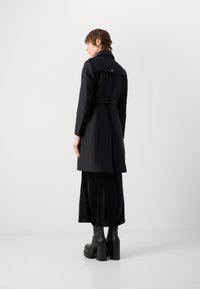 Manteau trench noir avec une taille ceinturée, des manches longues et un col montant. Le tissu semble lisse avec une silhouette structurée.