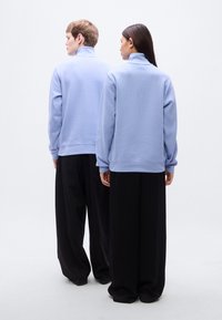 Ανοιχτό μπλε φλις πουλόβερ με ψηλό γιακά, συνδυασμένο με φαρδιά μαύρη παντελόνια. Μαλακή υφή, άνετη γραμμή, μινιμαλιστικός σχεδιασμός, χωρίς ορατά σχέδια.